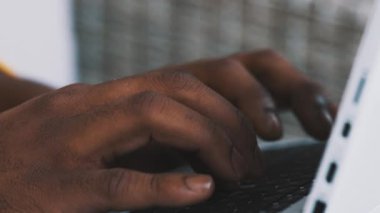 Laptop klavyesinde yazan Afrikalı Amerikalı siyahi bir adam. Uzak çalışma konsepti