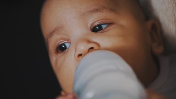 走近点，深色皮肤的婴儿手里拿着奶瓶喝牛奶 — 图库视频影像