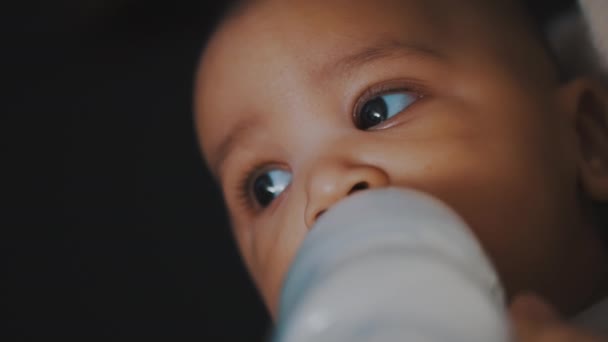 Retrato de un bebé multirracial bebiendo su fórmula de una botella de plástico. De cerca. — Vídeos de Stock