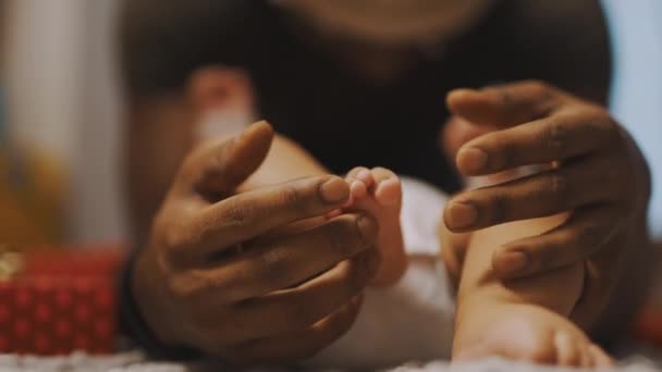 アフリカ系アメリカ人の父親が赤ん坊の足で遊んでいる。スローモーションを閉じます — ストック動画