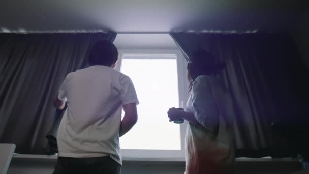 Jovem casal multirracial feliz em pé perto da janela e cortinas de abertura. Movimento lento — Vídeo de Stock