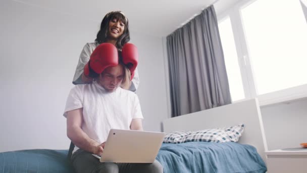 Mladá žena odvádí pozornost svého přítele od práce na laptopu. Hledač pozornosti s boxerskými rukavicemi — Stock video