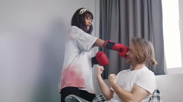 Junges Paar hat Spaß im Schlafzimmer. Frau schlägt ihrem Freund mit Boxhandschuhen ins Gesicht — Stockvideo