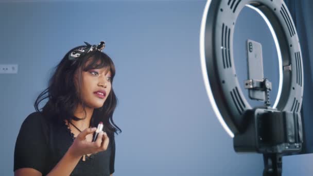 Młoda Afroamerykanka nagrywa film na swoim smartfonie oświetlony przez światło pierścienia podczas stosowania szminki — Wideo stockowe