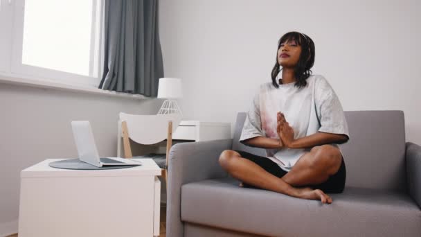 Meditáció és odafigyelés. Fiatal lelki fekete nő ül a kanapén meditálva vagy imádkozva — Stock videók