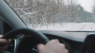 Driving the car on the snow covered road surrounded by tall leafless trees. Point of view shot