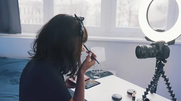 Zadní pohled na mladou ženu s černými vlasy nahrávání make-up tutorial. Aplikace make-upu před kamerou — Stock fotografie