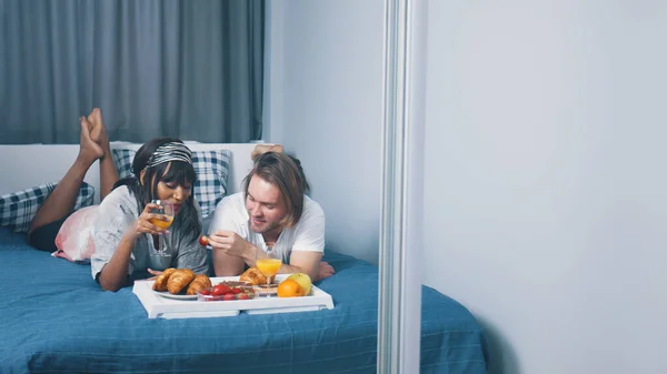 Mladý multiraciální pár odpočívá v ložnici a snídá v posteli. Zpomalený pohyb — Stock fotografie