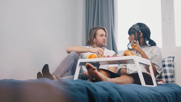 Lazy matin au lit. Jeune couple multiethnique buvant du jus de fruits et prenant un petit déjeuner dans la chambre — Photo