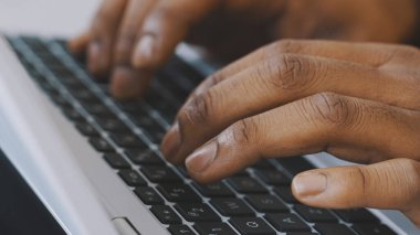 Laptop klavyesinde yazı yazan tanınmayan Afro-Amerikan iş adamının yakın çekim görüntüleri.