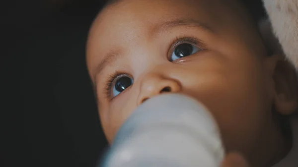 Beautiful mulatto baby dringking his formula milk from the bottle in the hands of his mom — Stock Photo, Image