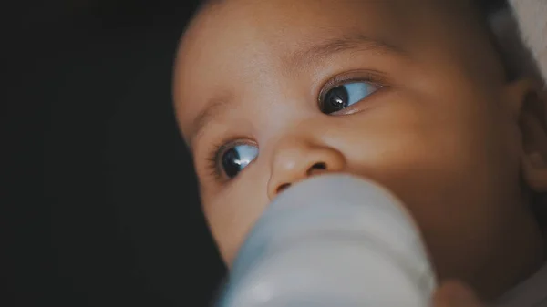 Adorable dark skin multiracial baby drinking his formula milk from the bottle in the hands of his mom — Stock Photo, Image