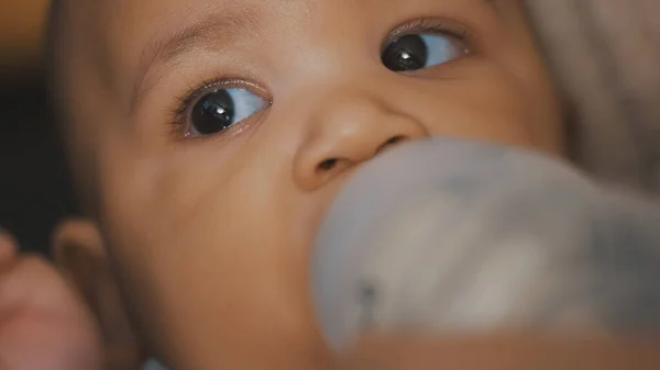 Close up, dark skin baby drinking milk from the bottle in mothers hands — Stock Photo, Image