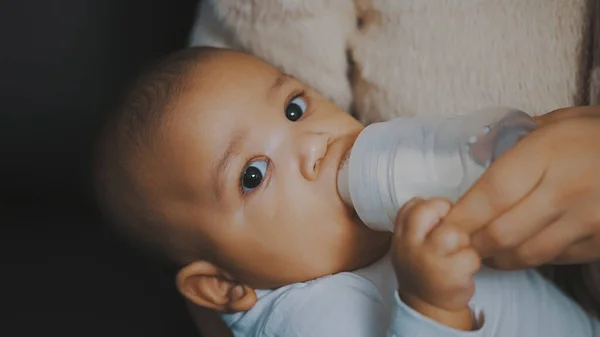 Close up adorable dark skin baby drinking his milk from the bottle in mothers hands — Stock Photo, Image