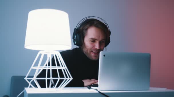 Fiatal fehér szakállas férfi fejhallgatóval videóhívással a laptopján — Stock videók