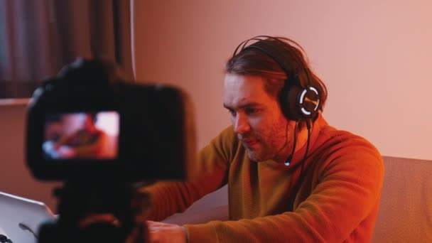 Jeune homme caucasien avec écouteurs travaillant sur ordinateur portable et enregistrement vidéo sur caméra dslr — Video