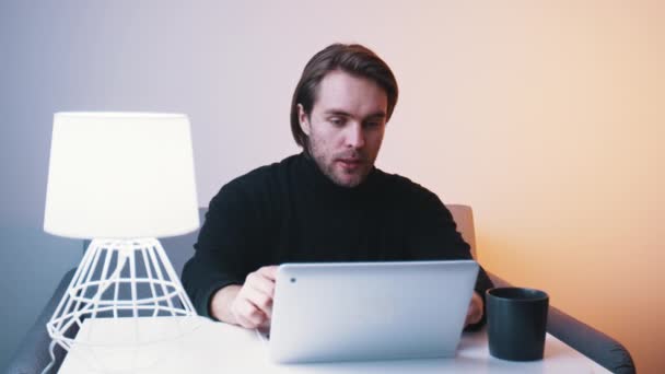 Молодий кавказький чоловік має відеоконференцію на ноутбуці в своїй квартирі — стокове відео