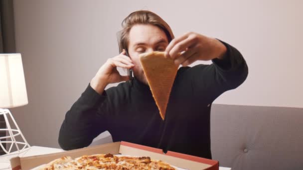 Un joven caucásico quejándose de pizza por teléfono. Sosteniendo una rebanada mientras usa el teléfono inteligente — Vídeo de stock