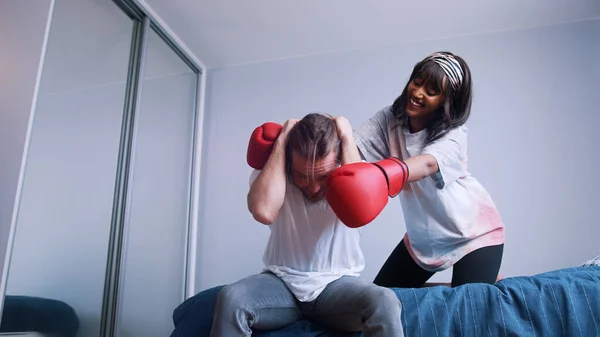 Heureux couple multiracial s'amuser dans la chambre à coucher. Jeune femme attaquant son petit ami avec des gants de boxe — Photo