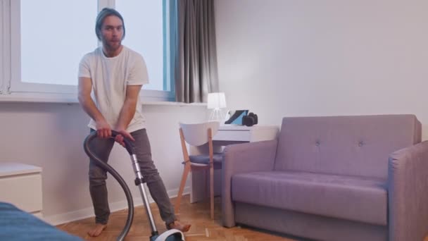 Jeune homme caucasien s'amusant pendant le nettoyage de la maison, jouer avec l'aspirateur au salon — Video