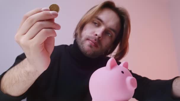 Portrait of young caucasian man putting coins in the piggy bank. Savings concept — Stock Video