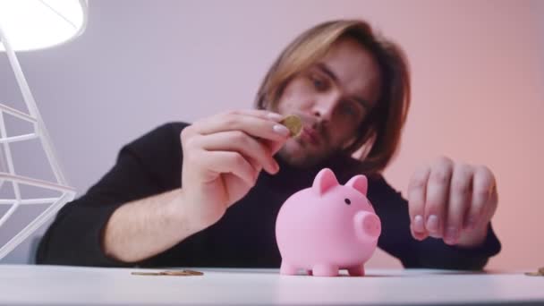 Retrato de un joven caucásico poniendo monedas en la alcancía. Concepto de ahorro — Vídeos de Stock