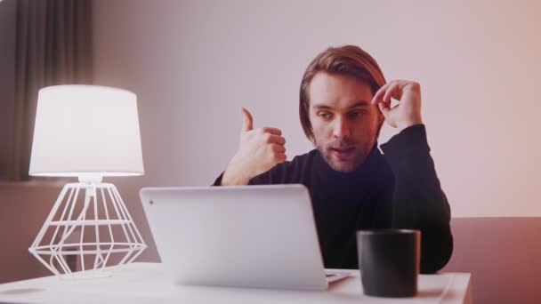 Fiatal kaukázusi férfi mutatja hüvelykujját felfelé és hüvelykujját lefelé, miközben egy videó hívás a laptopján — Stock videók