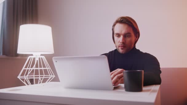 Caucásico hombre usando el ordenador portátil en casa con una taza de café cerca — Vídeos de Stock