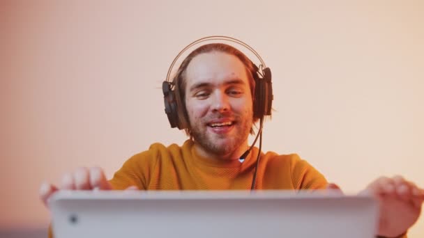 Porträtt av en ung man med hörlurar som vinner spelet. Spel som spelas på bärbar dator — Stockvideo