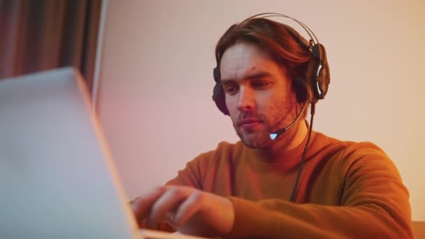 Porträtt av en ung man med headset som arbetar på laptop. Fjärrstyrt arbete — Stockvideo