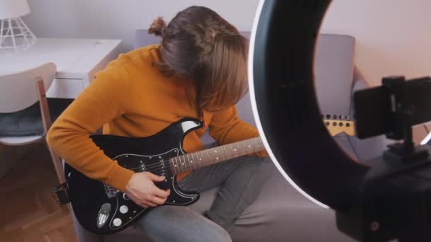 Junger Kaukasier spielt Gitarre und nimmt sie mit dem Smartphone auf. Streaming in den sozialen Medien — Stockvideo