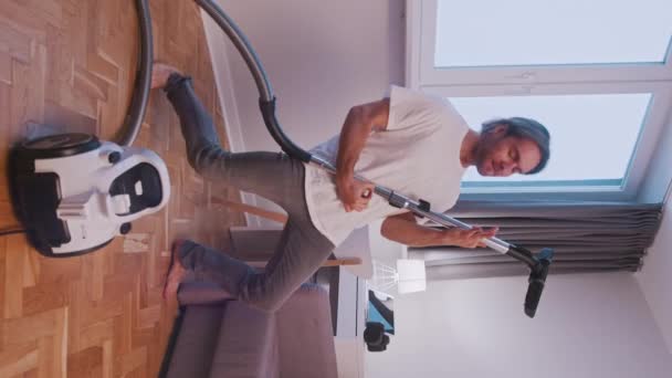 Lodret. Ung kaukasiske mand rengøring hus og bruge støvsuger som guitar – Stock-video