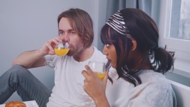 여러 인종으로 구성 된 젊은 남녀가 오렌지 주스를 마시고 침대에서 대화를 나누다 — 비디오