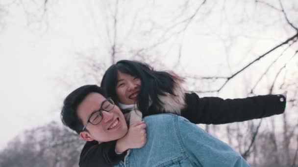 Jovem dando passeio de piggyback para sua namorada no parque no dia de inverno nevado. recém-casado asiático casal ter diversão fora — Vídeo de Stock