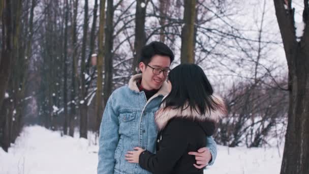 快乐的年轻的亚洲夫妇在雪地覆盖的树下接吻。冬季的爱情和感情。情人节 — 图库视频影像