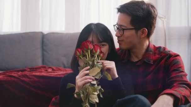 Boldog ázsiai pár, akik Valentin napot töltenek otthon. Szerelem és szeretet koncepció. Nő kezében csokor vörös rózsa — Stock videók