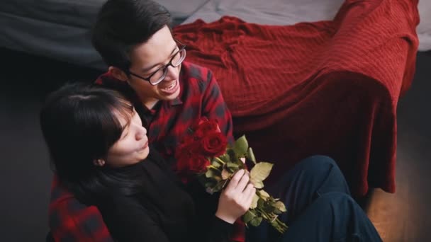 Boldog fiatal pár ünnepli évfordulóját az új lakásban. Ázsiai nő kezében csokor vörös rózsa — Stock videók