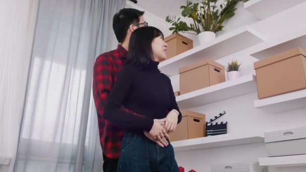 Młoda szczęśliwa para wprowadza się do nowego mieszkania. Przytulanie się do półki z kartonowymi pudełkami — Wideo stockowe