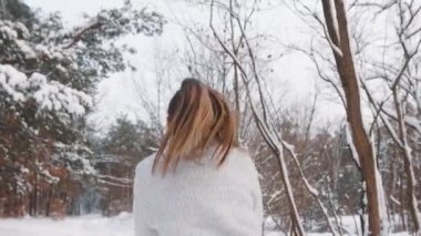 Genç bir kadın parkta zıplayıp başının üstüne kar fırlatıyor. Kış mevsimi