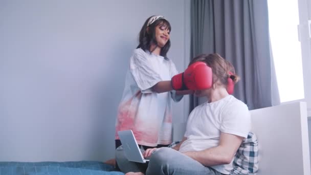 Genç çok ırklı çift yatakta eğleniyor. Erkek arkadaşını yumruklayan boks eldivenli bir kadın. — Stok video