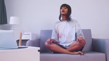 Afro-Amerikalı kadın kanepesinde meditasyon yapıyor. Derin nefes alma tekniği. Sağlıklı yaşam tarzı