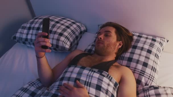Jovem entediado solitário homem segurando smartphone em sua cama — Vídeo de Stock