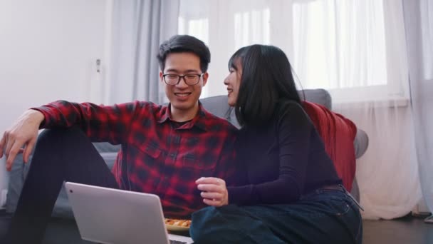Ευτυχισμένο νεαρό ζευγάρι χαλαρώνει στον καναπέ αγκαλιάζοντας και βλέποντας ταινία στο laptop — Αρχείο Βίντεο
