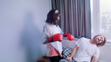 Genç çift yatak odasında eğleniyor. Erkek arkadaşının suratına boks eldiveniyle yumruk atan bir kadın.