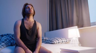 Yatakta oturan genç beyaz bir adam. Uykusuzluk, zihinsel bozukluk ya da depresyon