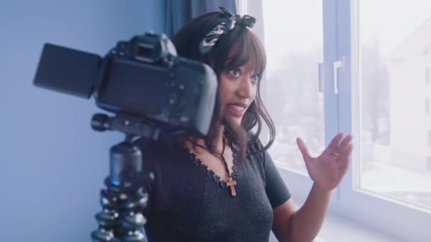 젊은 여성 블로거가 창문 근처에 서 있는 동안 카메라를 들고 vlog 를 위한 비디오 녹화를 하는 모습 — 비디오