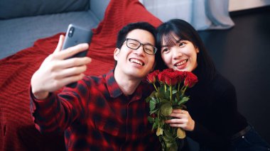 Mutlu genç Asyalı çift selfie çekiyor. Kırmızı güller tutan kadın