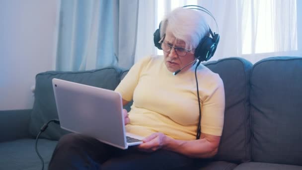 Starší žena se sluchátky hrát videohry na notebooku — Stock video