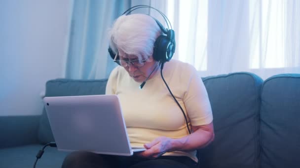 Starší žena se sluchátky má videohovor s rodinou. Staří lidé a technologie — Stock video