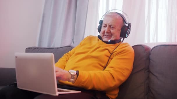 Dědeček se sluchátky hrát hry na notebooku — Stock video